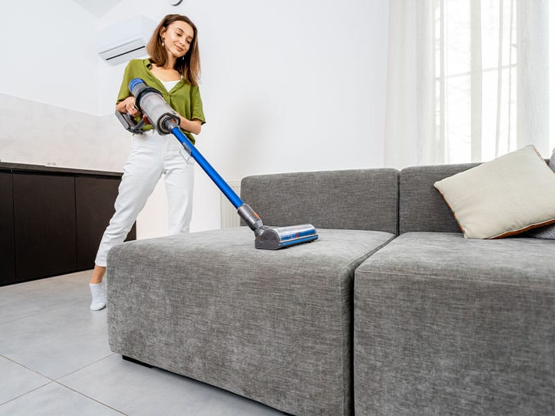 Woman cleaning sofa with a cordless vacuum